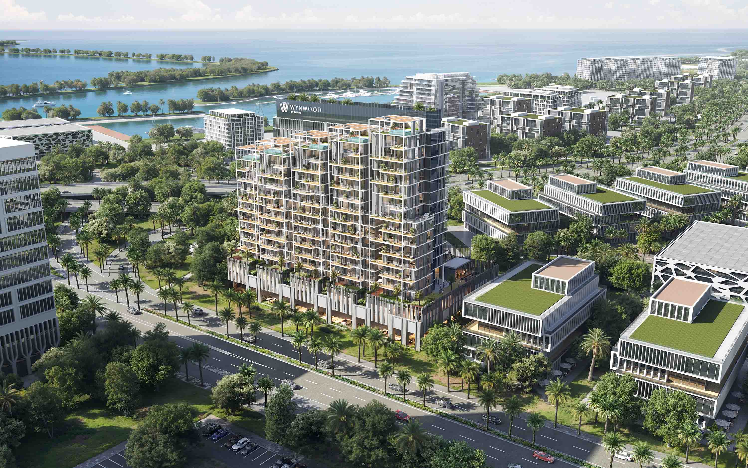 Wynwood By Imtiaz Aerial view of a modern building complex with greenery, palm trees, and a waterfront in the background.